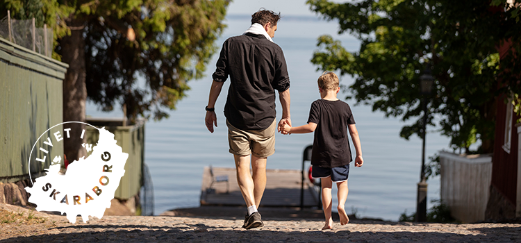 Far och son går längst kullerstensgata mot sjö