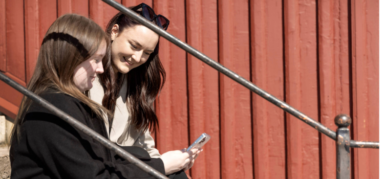 Kvinnor sittandes i trappa tittandes på en mobiltelefon