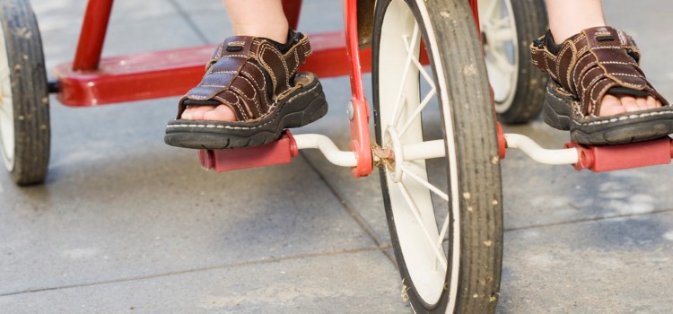 Framhjulet på en trehjuling och barnfötter på pedalerna